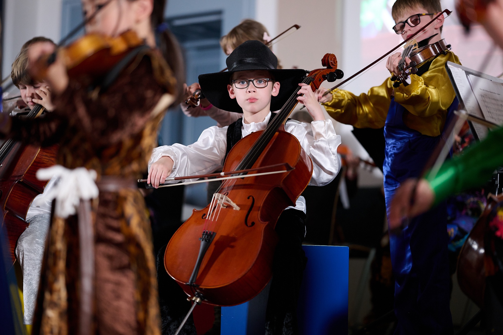 Ein Junge mit schwarzem Hut und Brille spielt konzentriert Cello im Ensemble