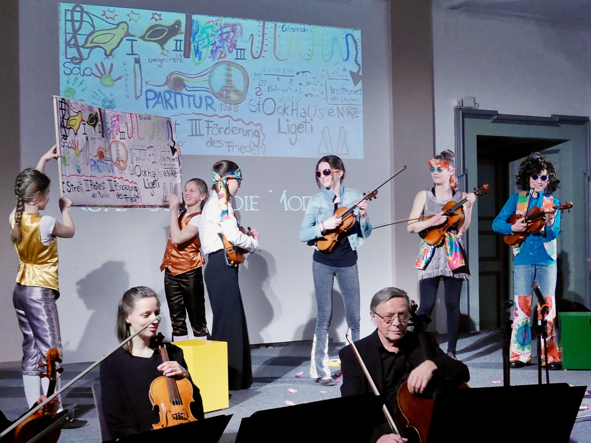 Eine farbenfrohe KinesisGruppe gestaltet mit Instrumenten, Kostümen und einem gemeinsamen Plakat eine Bühnenszene