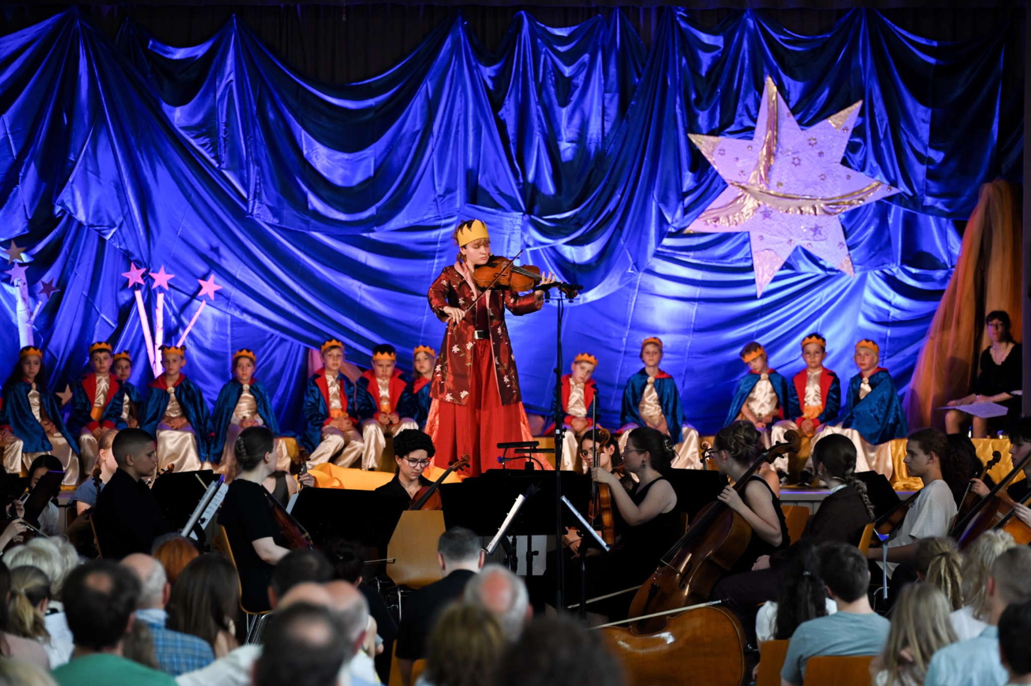 Eine Geigerin spielt als Solistin mit Orchester und einer szenisch gestalteten Kindergruppe auf der Bühne